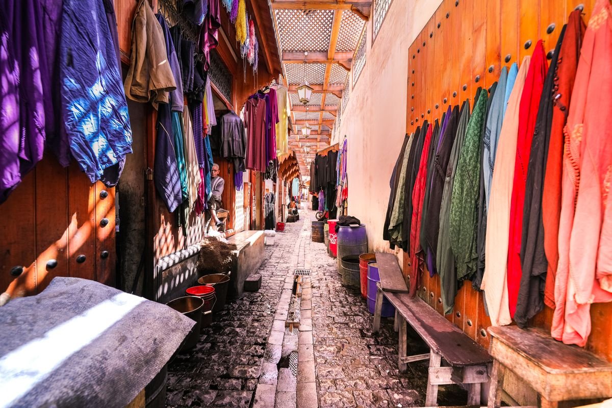 A narrow souk alley in Morocco lined with clothing and goods for sale